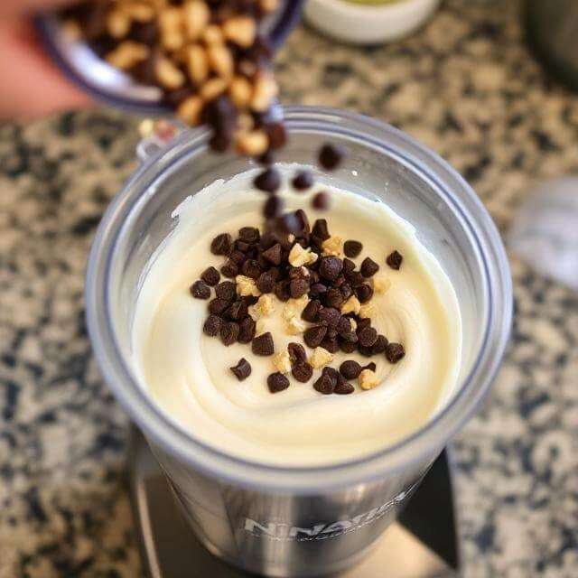 A variety of optional mix-ins like dark chocolate chunks, chopped almonds, and fresh berries being folded into protein ice cream base.