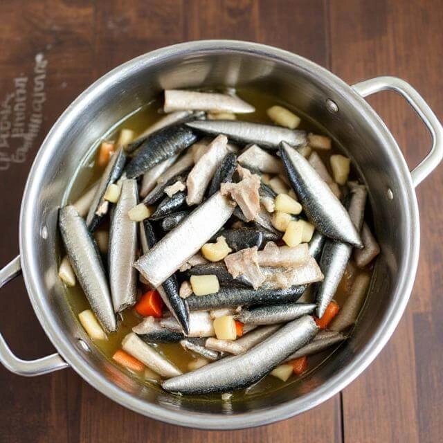 Canned sardines being added to a skillet with sautéed garlic and spinach, then gently broken apart with a spoon.

