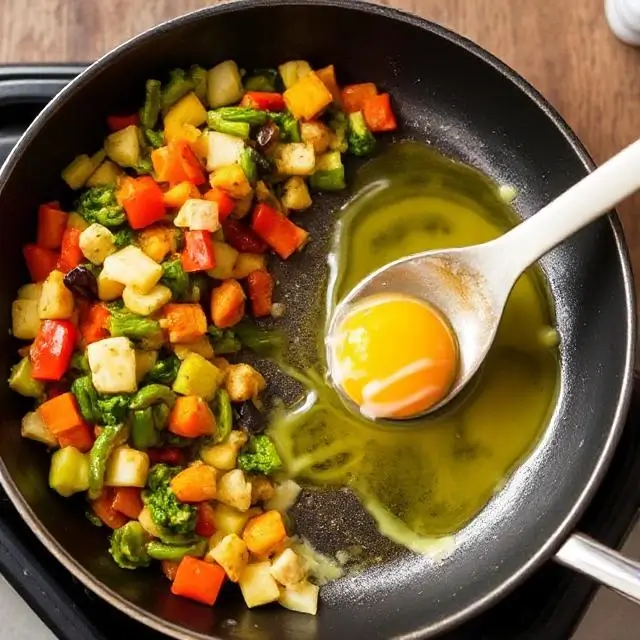 Beaten eggs cooking beside sautéed vegetables in a skillet.
