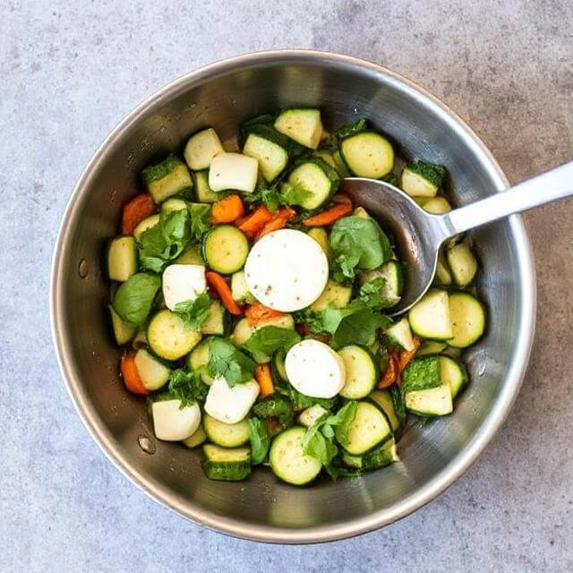 Zucchini slices and fresh basil sautéing in olive oil in a skillet.

