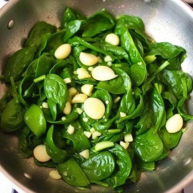 Garlic and fresh spinach sautéing in olive oil in a skillet.