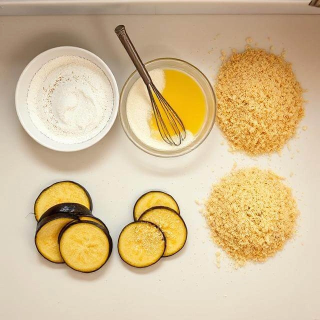 Eggplant slices being coated with breadcrumbs in preparation for frying
