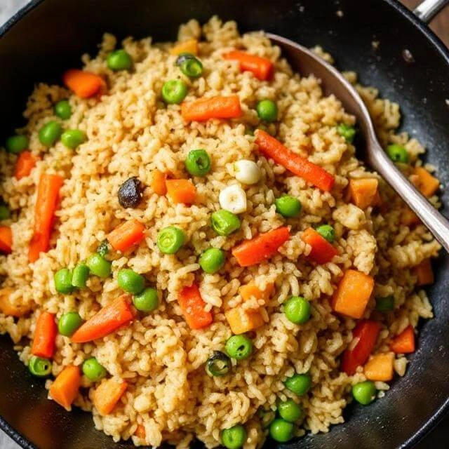 Egg fried brown rice mixed with colorful vegetables such as carrots, peas, and green onions in a skillet.