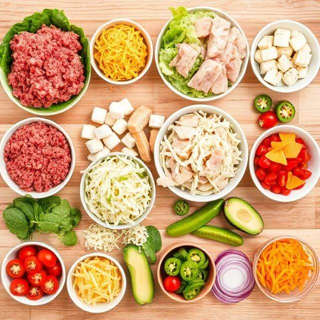 Fresh ingredients for a high-protein burger bowl including grilled chicken, lean beef, veggies, and Greek yogurt sauce