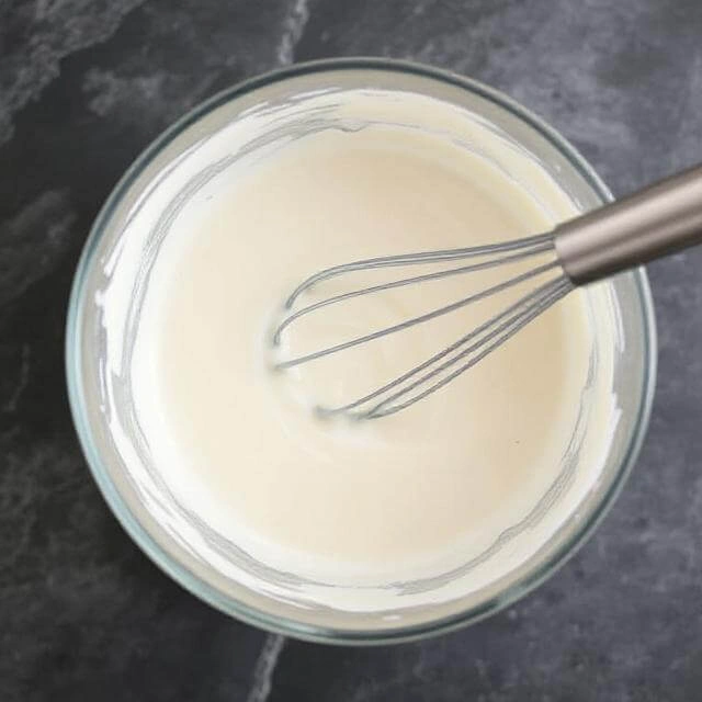 Pouring almond milk into protein ice cream base mixture in stainless steel bowl